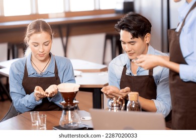 Young man and woman learning making coffee and sniff bean with barista while laptop on desk at cafe, group people training drip coffee with entrepreneur, small business or SME.