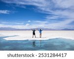 Young man and woman in love posing in the Salinas Grandes of Argentina during their vacation at the edge of a blue lake in which they are reflected