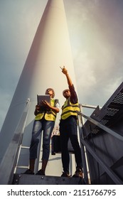 Young Man And Woman Maintenance Engineer Team Working And Holding The Report In Wind Turbine Farm. Generator Station, Renewable Energy