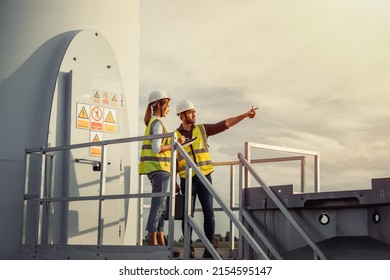 Young Man And Woman Maintenance Engineer Team Working And Holding The Report In Wind Turbine Farm. Generator Station, Renewable Energy