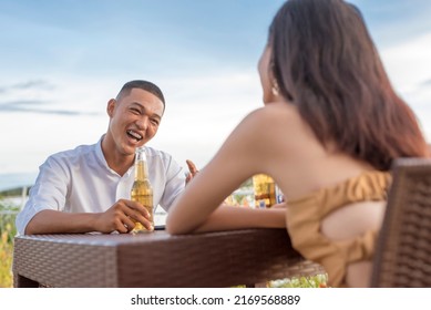 A young man and woman on a first date going very well. A couple laughing and having a great time while drinking beer at an outdoor cafe or bar during the late afternoon. Dating chemistry concept.