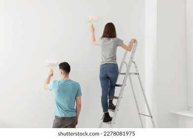 Young man and woman painting wall with rollers indoors. Room renovation - Powered by Shutterstock