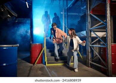 young man and woman running from scary people in gas masks and orange ppe suits in escape room