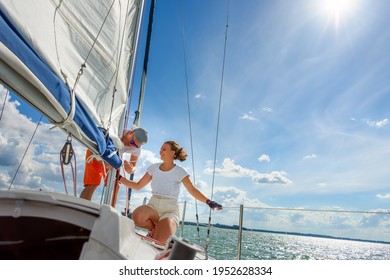 Young Man And Woman Sailing On A Yacht. Female Sailboat Crewmember Trimming Main Sail During Sail On Vacation In Summer Season