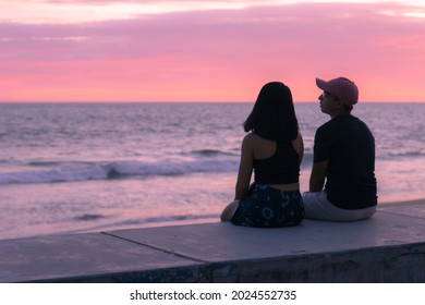 Young man and young woman sitting enjoying the sunset. Brother and sister relaxing near the beach