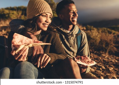 Young Man And Woman Sitting On Mountain Trail Eating Pizza And Looking At The View. Couple On Hiking Trip Eating Pizza And Admiring The View.