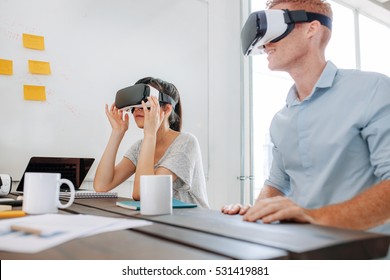 Young Man And Woman Sitting At A Table And Using Virtual Reality Goggles. Business Team Using Virtual Reality Headset In Office Meeting.