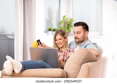 Young Man And Woman Sitting Together On Couch With Feet Up. Couple Using Laptop For Online Shopping.  