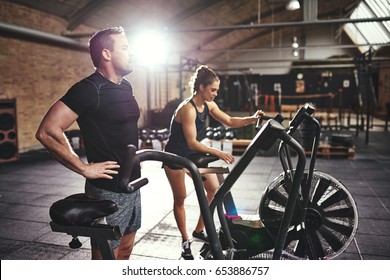 Young man and woman in sportive outfit having rest after riding cycling machines in light spacious gym. 