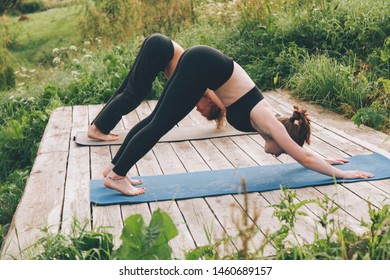 Young Man And Woman Stand In Dog Yoga Pose Outside. Barefeet Couple Exercising On Fresh Air. Stand On Blue Mat. Flexible Young People Have Workout