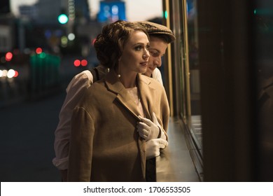 A young man and woman stand near a glass shop window and look at it. In retro suits. Historical reconstruction.
