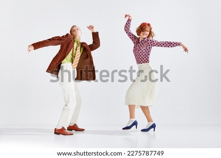 Young man and woman in stylish colorful clothes dancing retro dance against grey studio background. Active hobby. Concept of art, retro style, hobby, party, fun, movements, 60s, 70s culture