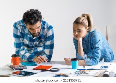 Young man and woman together working at design project. Creative teamwork at workspace with construction blueprint and color swatches. People standing near desk and discussing in architecture studio