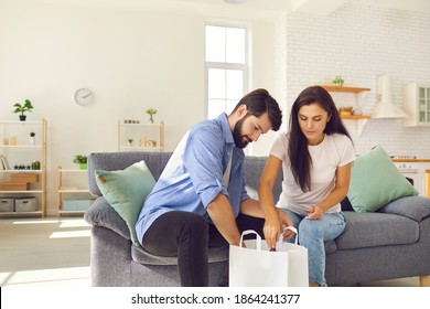 Young man and woman unpack a white bag of groceries delivered to them by the home delivery service. Couple sitting on sofa in living room and enjoying modern service. Food delivery concept. - Shutterstock ID 1864241377