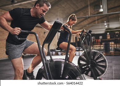 Young man and woman wearing training hardly on cycling machines in light spacious gym. - Powered by Shutterstock