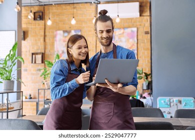 Young man and woman workers owners in aprons using laptop, inside restaurant cafe - Powered by Shutterstock