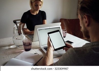 Young Man And Young Woman Working Opposite Each Other With Laptops. Male Person Using Digital Tablet With Blank Copy Space Screen For Your Information