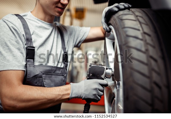 A young man is at work changing a tire on a\
lifted car. Vehicle\
maintenance