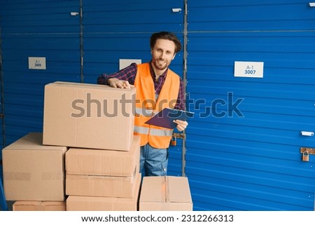 Young man in work clothes with boxes into warehouse with self storage unit