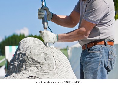 Young Man At Work With Compressed Air Chisel And Protective Gloves To Carving A Stone Block