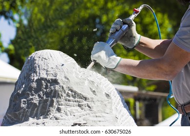 Young Man At Work With Compressed Air Chisel And Protective Gloves To Carving A Stone Block