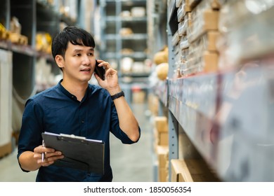 young man worker talking on a mobile phone and holding clipboard to checking inventory in the warehouse store - Powered by Shutterstock