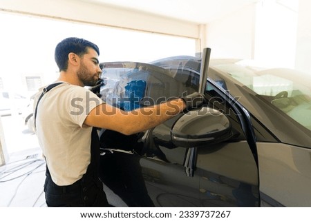 Young man working at the auto detail service measuring tinting film of vehicle window glass