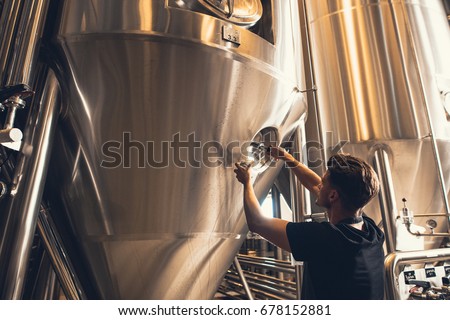 Young man working in beer manufacturing factory. Brewer working with industrial equipment at the brewery.