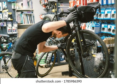 Young man working in a biking repair shop under quarantine and pandemic coronavirus in a protective mask on the face. Bicycle Mechanic Repair Bike, Cycle Workshop in medical mask covid 19 - Powered by Shutterstock