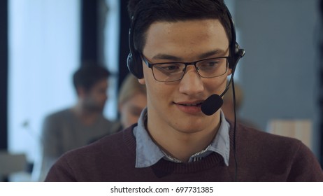 Young man working at a computer in a call centre smiling