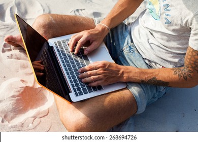 Young  man working with computer on the beach. Handsome man working with laptop laying on the couch at the beach. Empty display for your screen shot.