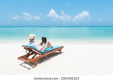 Young man working as digital nomad on the beach with a laptop