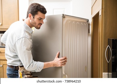 Young Man Working As An Electrician Exposing The Back Of A Fridge To Check And Repair It