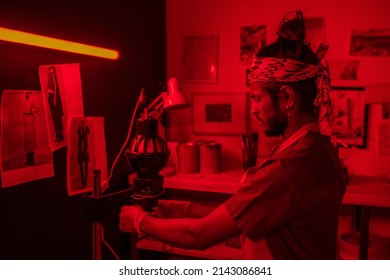 Young man working with film photography in red lit darkroom using photo enlarger to project image onto paper - Powered by Shutterstock