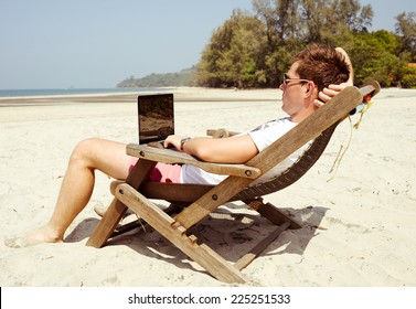 Young Man Working With Laptop In A Beach