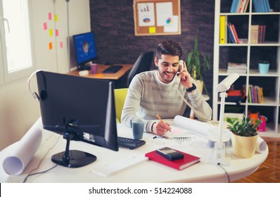 Young Man Working On Computer Talking On Land Line Phone