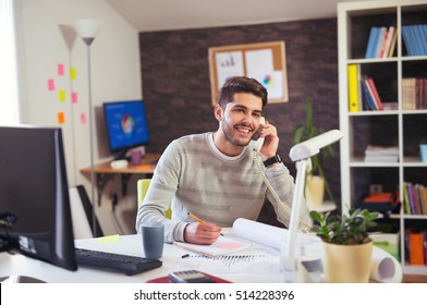 Young Man Working On Computer Talking On Land Line Phone