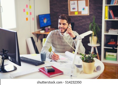 Young Man Working On Computer Talking On Land Line Phone