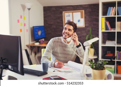 Young Man Working On Computer Talking On Land Line Phone