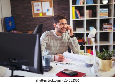 Young Man Working On Computer Talking On Land Line Phone