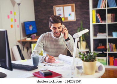 Young Man Working On Computer Talking On Land Line Phone