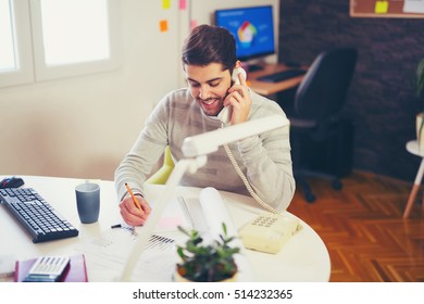 Young Man Working On Computer Talking On Land Line Phone