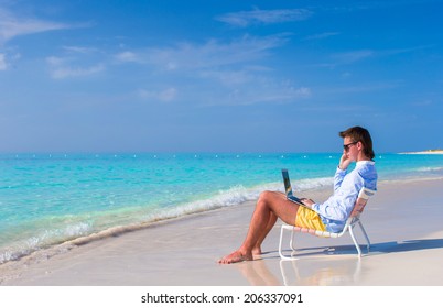 Young man working on laptop at tropical beach - Powered by Shutterstock