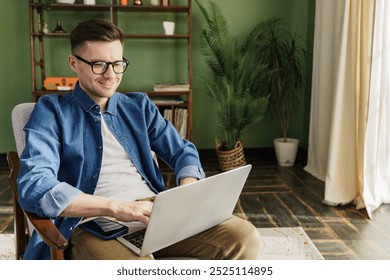 Young Man Working on a Laptop in a Cozy Home Office With Green Walls and Natural Light Coming From the Window - Powered by Shutterstock