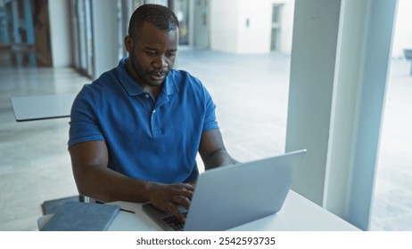 Young man working on laptop in an office setting with a focused expression on his face, suggesting a professional environment. - Powered by Shutterstock