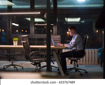 Young Man Working On Laptop At Night In Dark Office. The Designer Works In The Later Time.