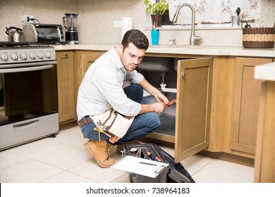 Young Man Working As A Plumber And Using A Wrench To Fix A Leaky Faucet In A Kitchen
