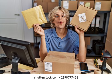 Young Man Working At Small Business Ecommerce Holding Packages Making Fish Face With Mouth And Squinting Eyes, Crazy And Comical. 