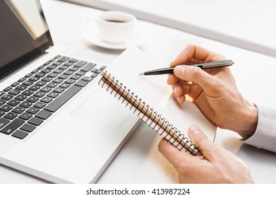 Young man is working, using laptop computer and writing in his notebook