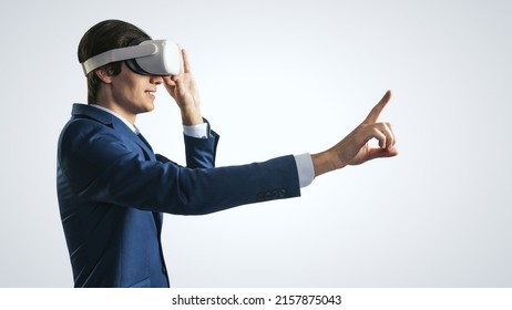 Young Man Working In Virtual Reality Office In VR Glasses, Presses His Finger Virtual Interface On Abstract Light Grey Backdrop. Innovate And Future Technology Concept, Close Up